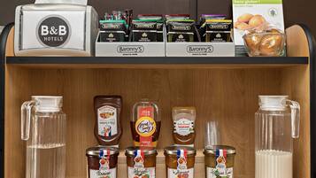 Ein Hôtelminikühlschrank mit verschiedenen Lebensmitteln und Getränken, darunter Gläser mit Marmelade, Honig und eine Karaffe Wasser.