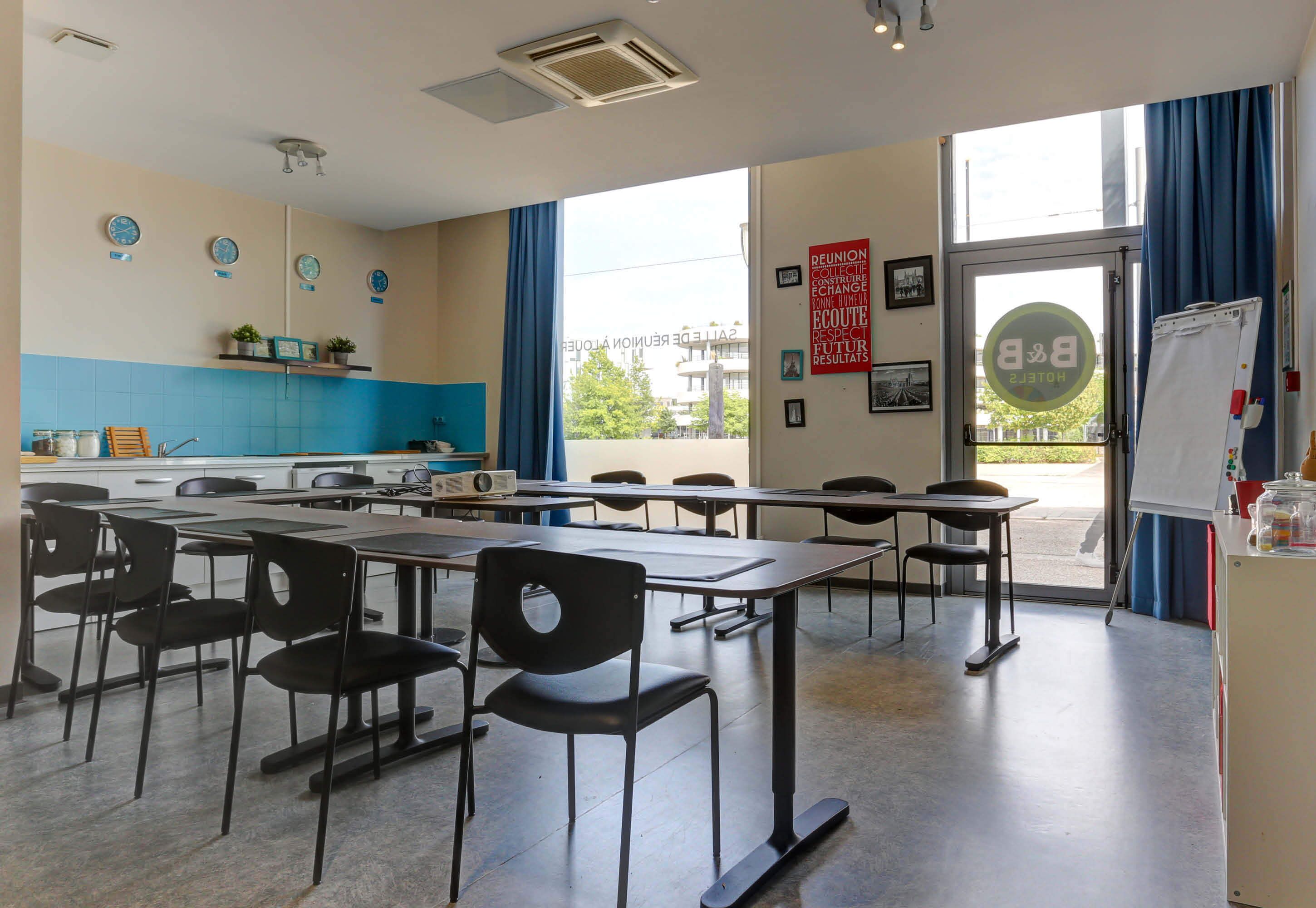 A classroom with tables and chairs, a whiteboard, and a window with curtains.