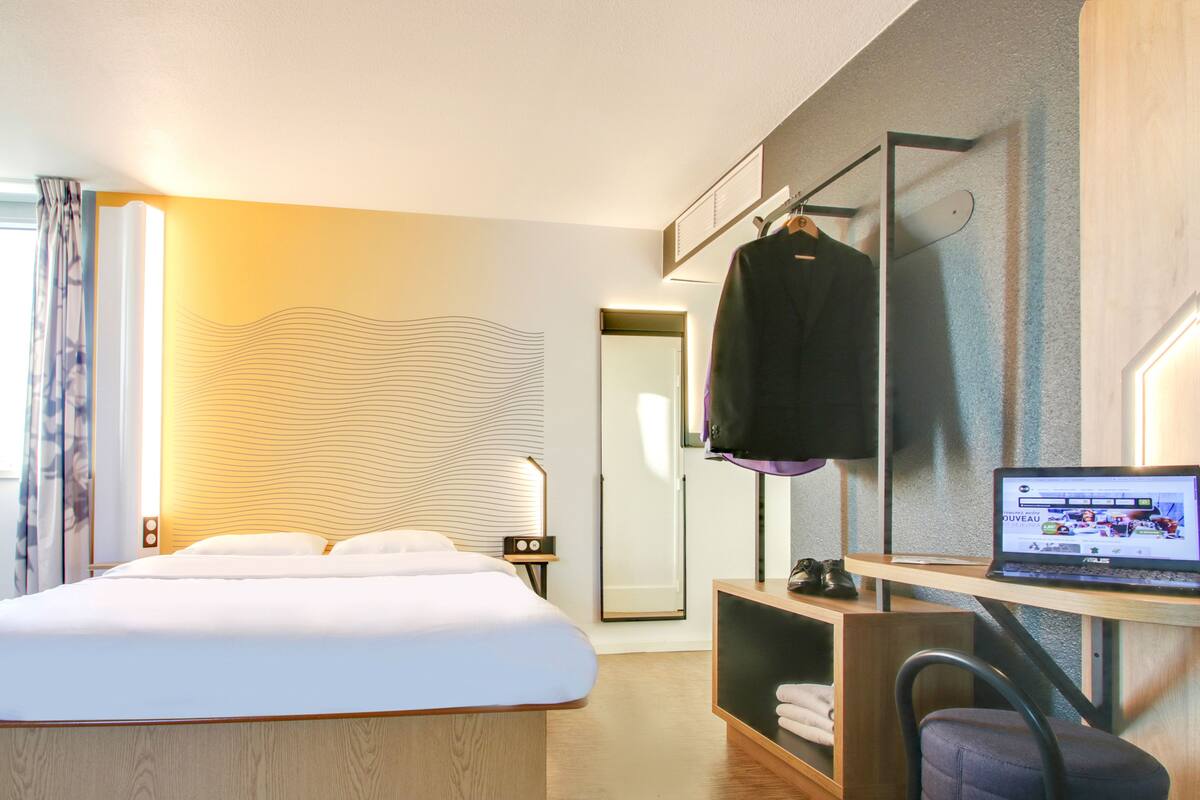Quarto de hotel moderno com uma cama grande, uma escrivaninha com um laptop e um espelho.
