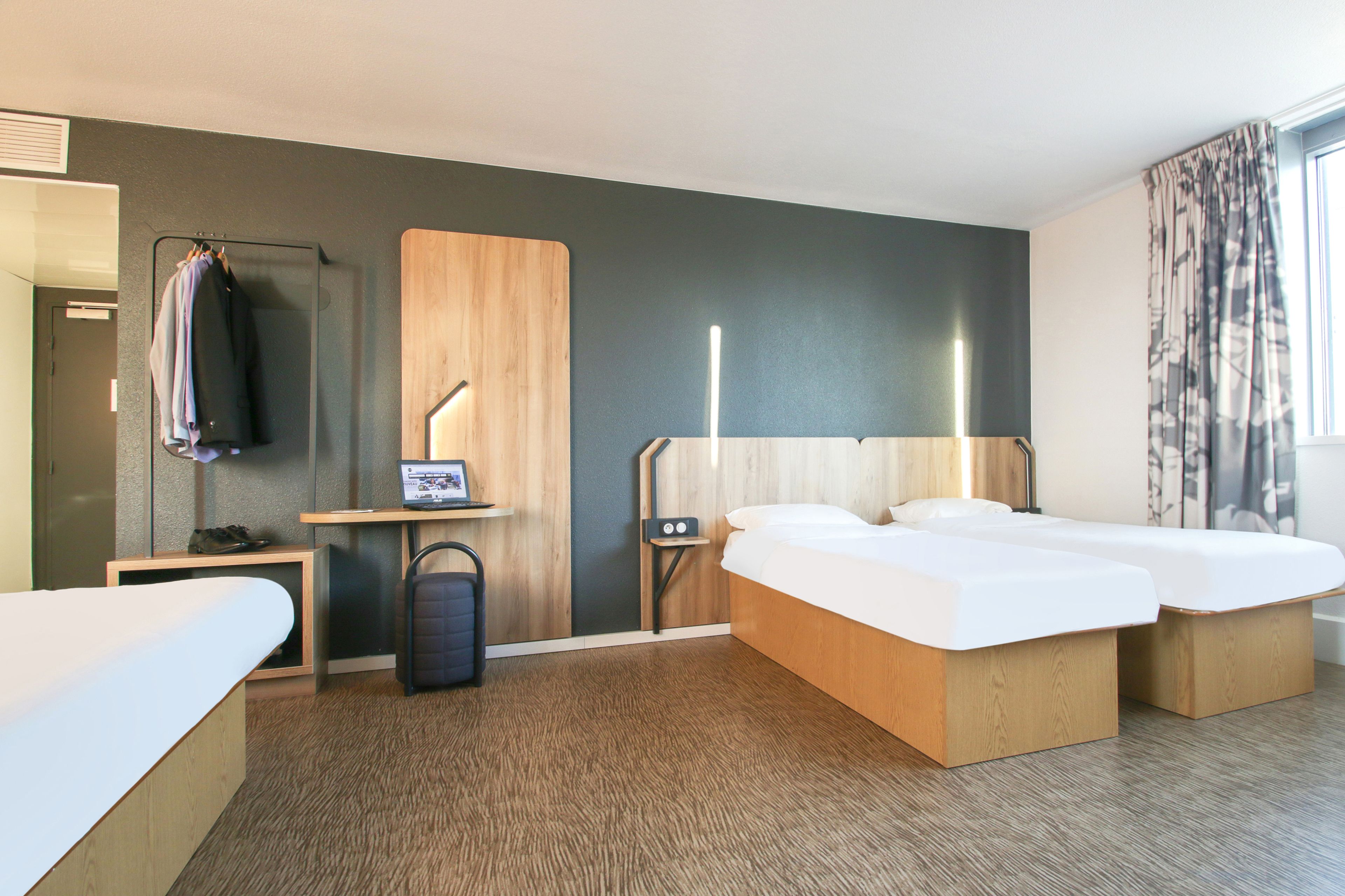 Quarto de hotel com cama, mesas de cabeceira, escrivaninha, cadeira, guarda-roupa e janela com cortinas.