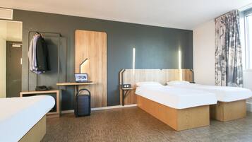 Quarto de hotel com cama, mesas de cabeceira, escrivaninha, cadeira, guarda-roupa e janela com cortinas.