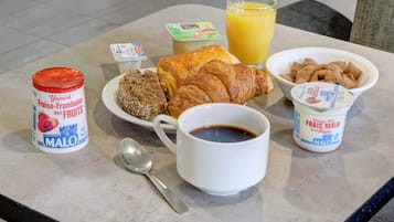 Una mesa de desayuno con un croissant, un tazón de cereal, un vaso de jugo de naranja, una taza de café y dos recipientes de yogur.