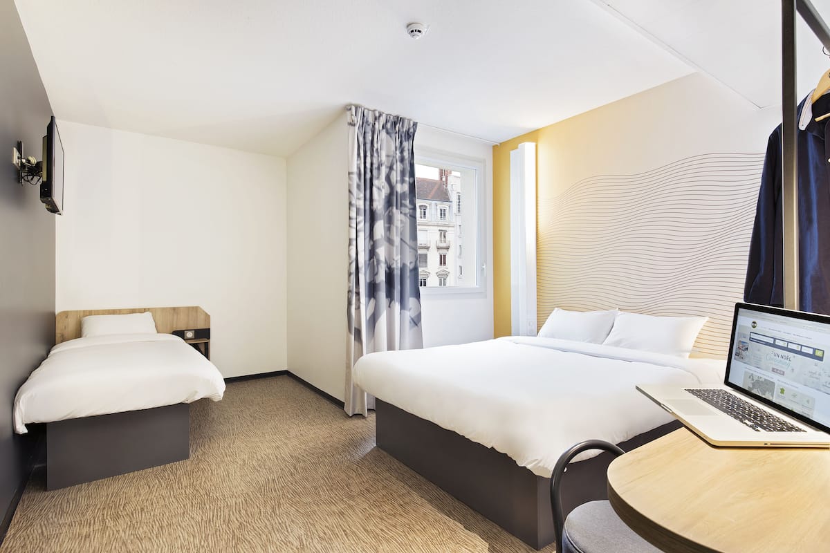 Quarto de hotel com duas camas, um laptop sobre uma mesinha e vista para edifícios.