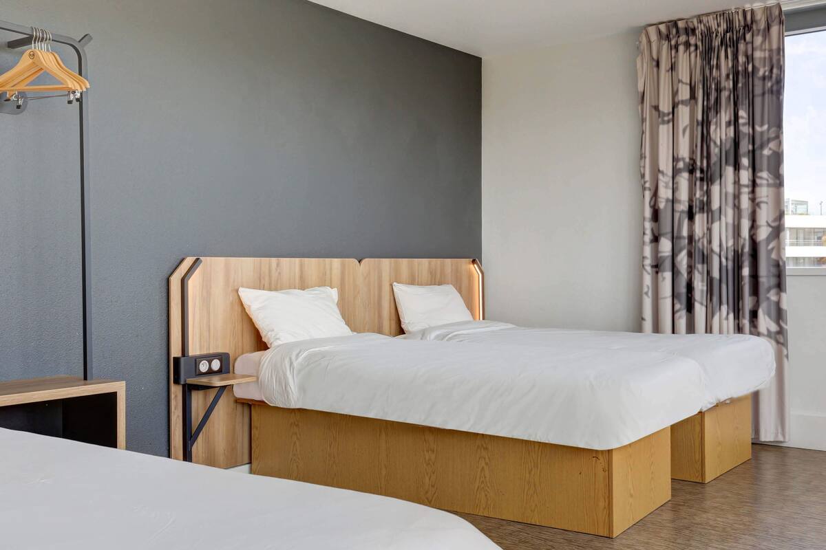 Quarto de hotel moderno com estrutura de cama de madeira, roupa de cama branca e parede cinza de destaque.