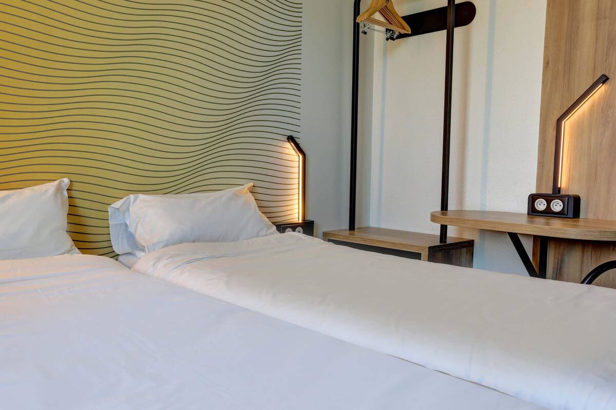 Quarto de hotel com cama, mesas de cabeceira, espelho e parede com padrão ondulado.