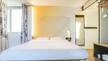 Une chambre d’hôtel moderne avec un grand lit, une table de chevet avec une lampe, un miroir et une armoire.
