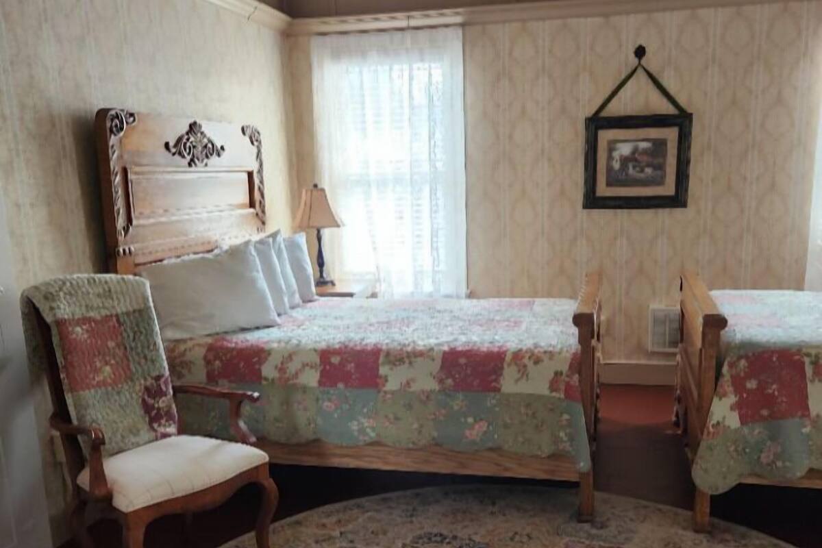 A bedroom with a bed, two chairs, a lamp, and a picture on the wall.