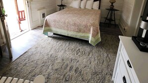 A bedroom with a wooden bed, a small bedside table with a lamp, a dresser, and a door leading to an outdoor area.