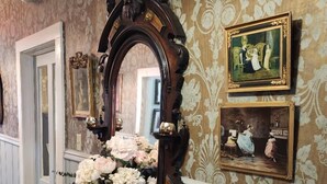 A vintage vanity with a mirror, a vase of flowers, and two framed paintings on the wall.