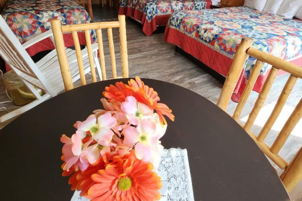 A wooden room with two beds, a table with a floral centerpiece, and a chair.