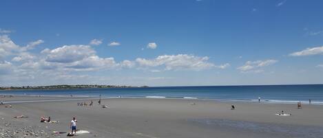 A wide beach with people sunbathing and swimming.