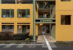 A multi-story hotel with a yellow facade, a visible entrance, and a sign reading 'B&B HOTELS.'