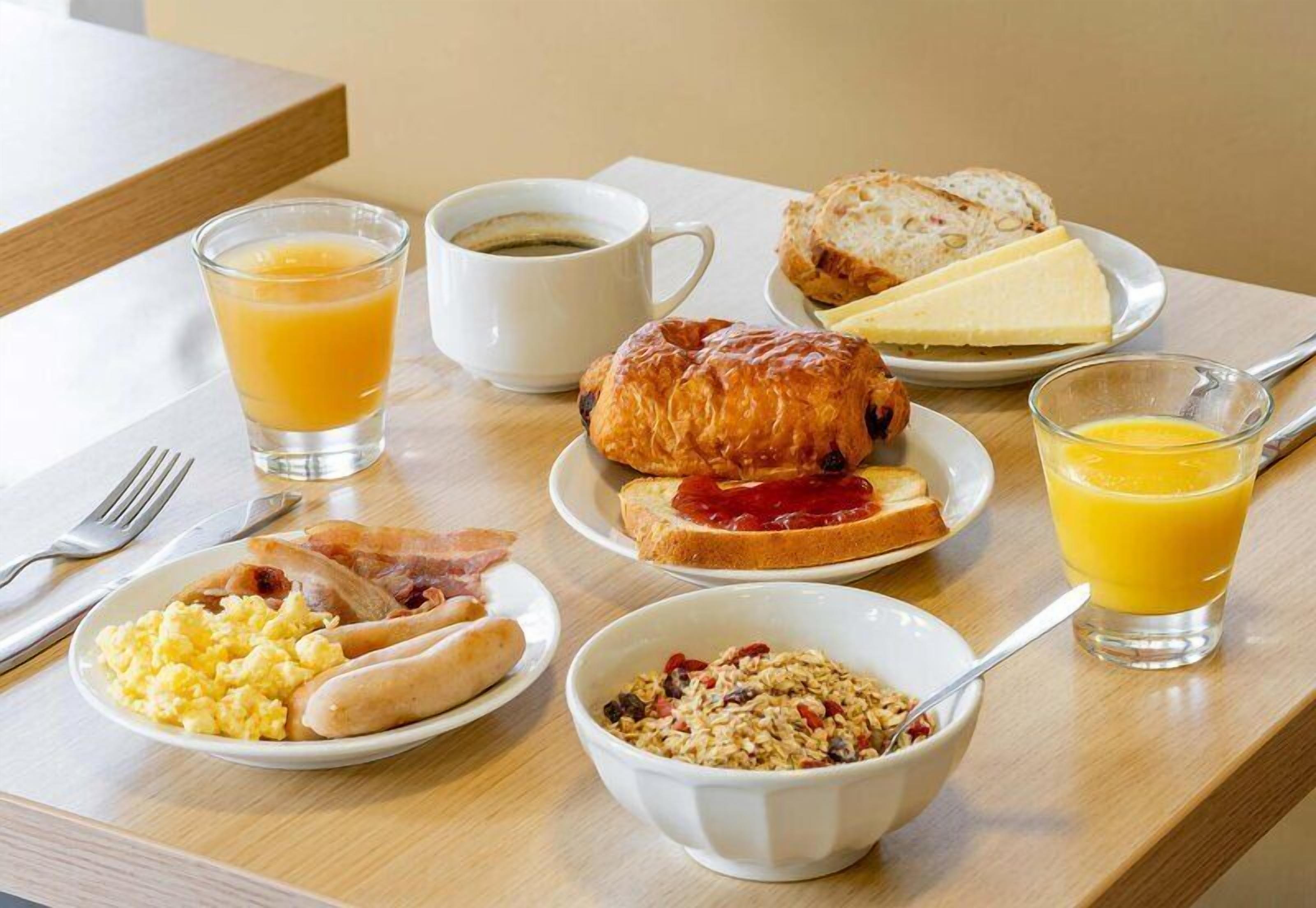 En frukostbricka med ägg, bacon, rostat bröd, croissant och juice.