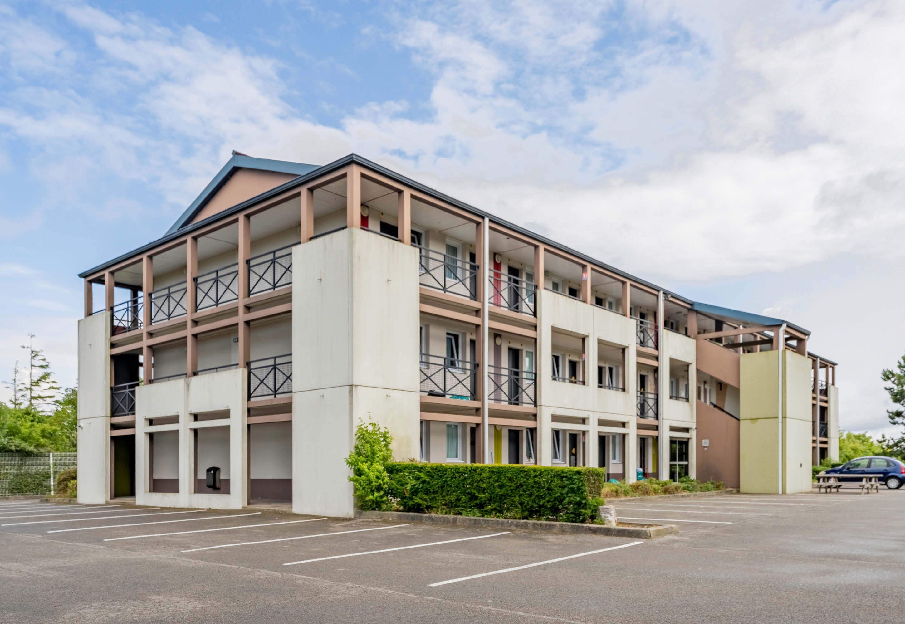 Ein mehrgeschossiges Gebäude mit flachem Dach, Balkonen und einem Parkplatz.