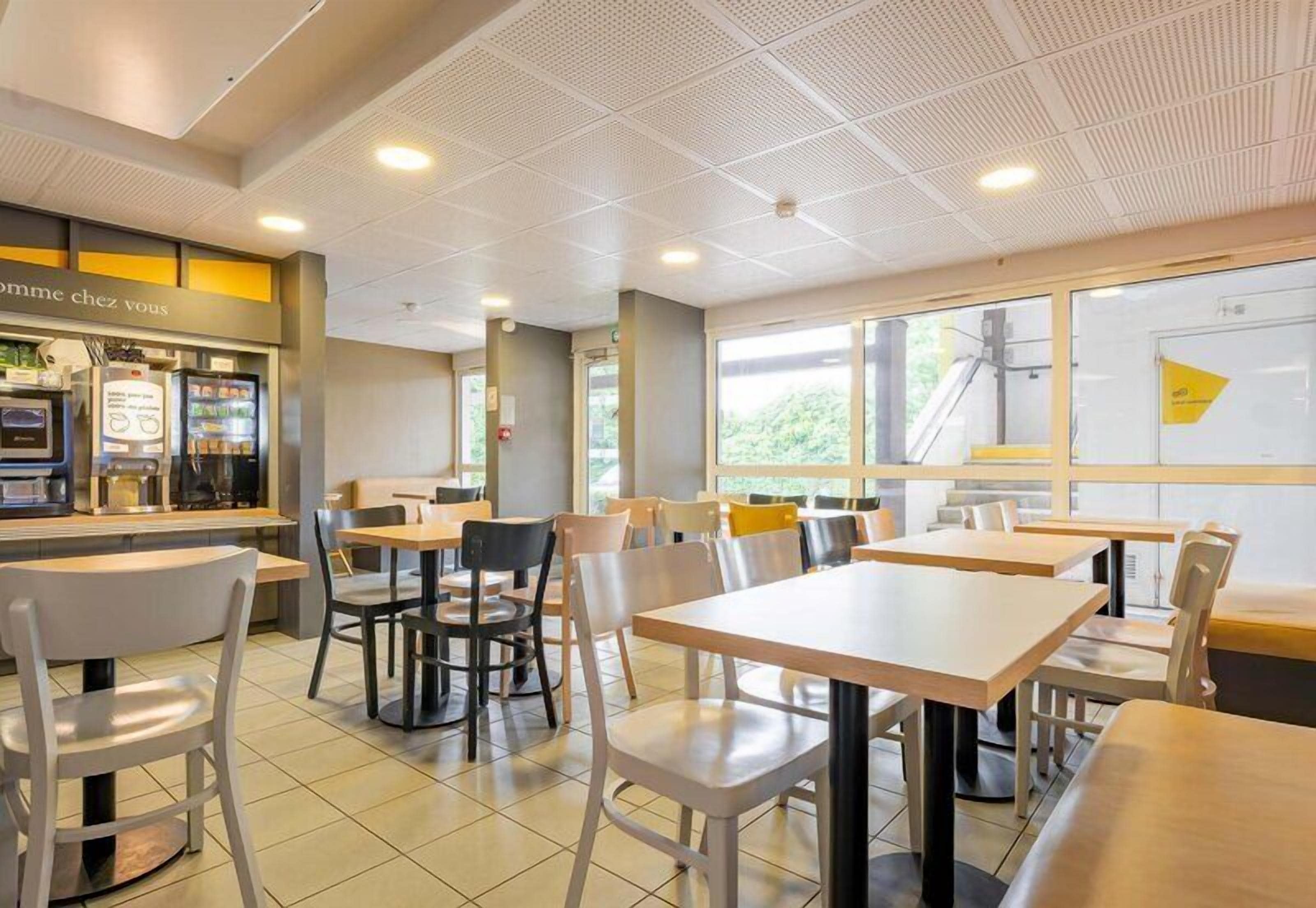 A modern cafe with tables and chairs, a counter with a menu, and large windows.