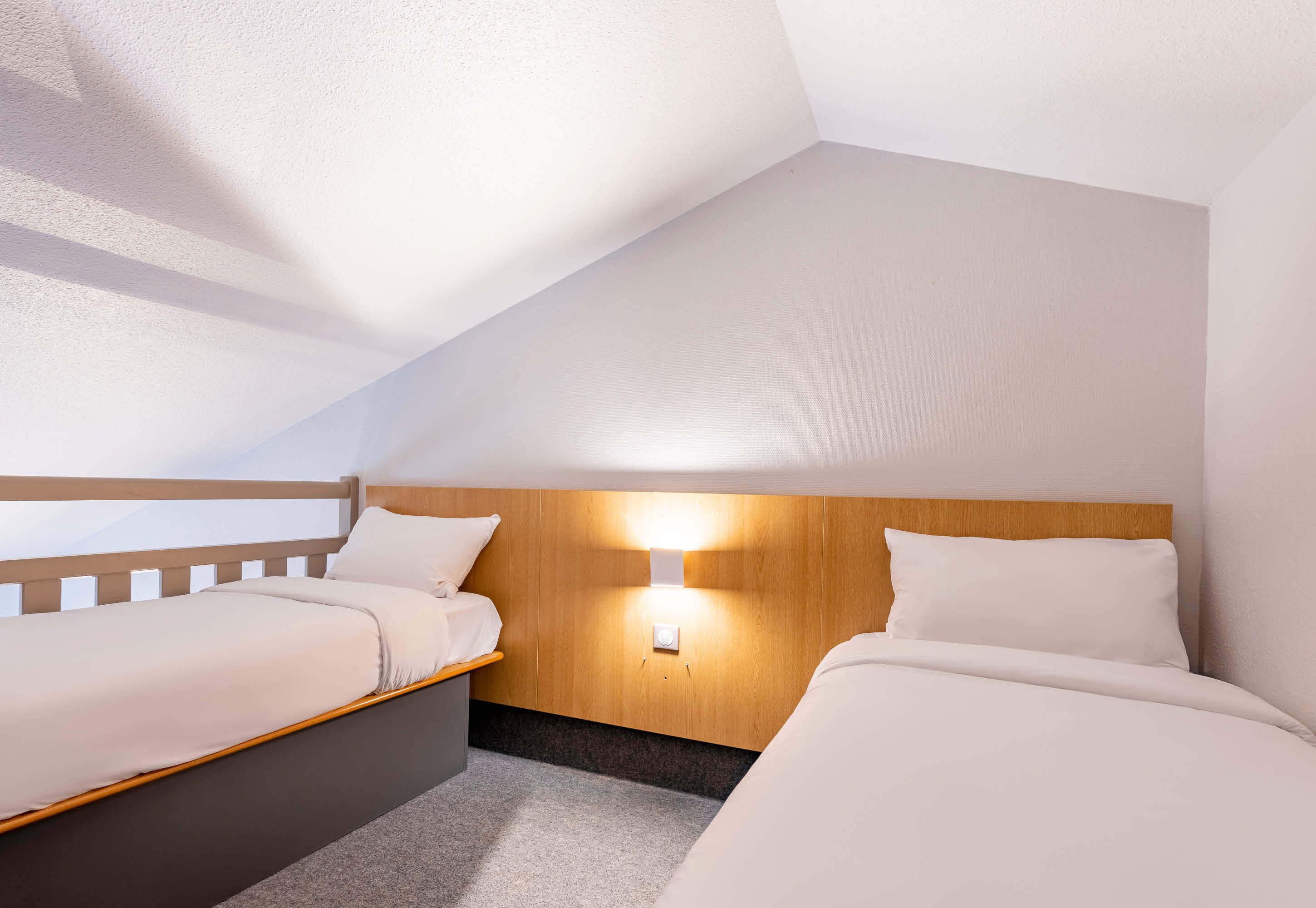 A room with two beds, a wooden headboard, a wall-mounted light, and a carpeted floor.