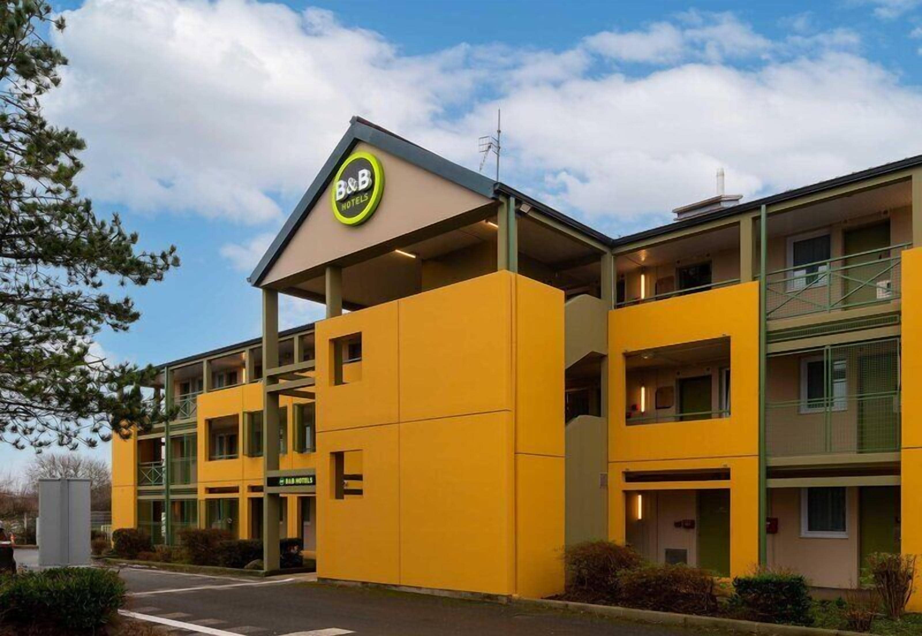 A yellow B&B hotel with a prominent sign, a covered entrance, and a two-story structure.