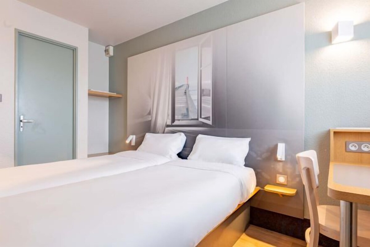 Une chambre d’hôtel avec un lit, une table de chevet et un petit bureau avec une chaise.