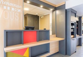 A reception desk with a laptop, a red accent, and a 'Bienvenue Chez Vous' sign.