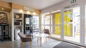 Eine Lobby mit Sitzgelegenheit, einem Verkaufsautomaten, einer Mikrowelle und einer Glastür zum Außenbereich.