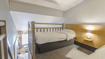Een slaapkamer met een stapelbed, een bureau met een laptop, een nachtkastje met een lamp en een raam met gordijnen.