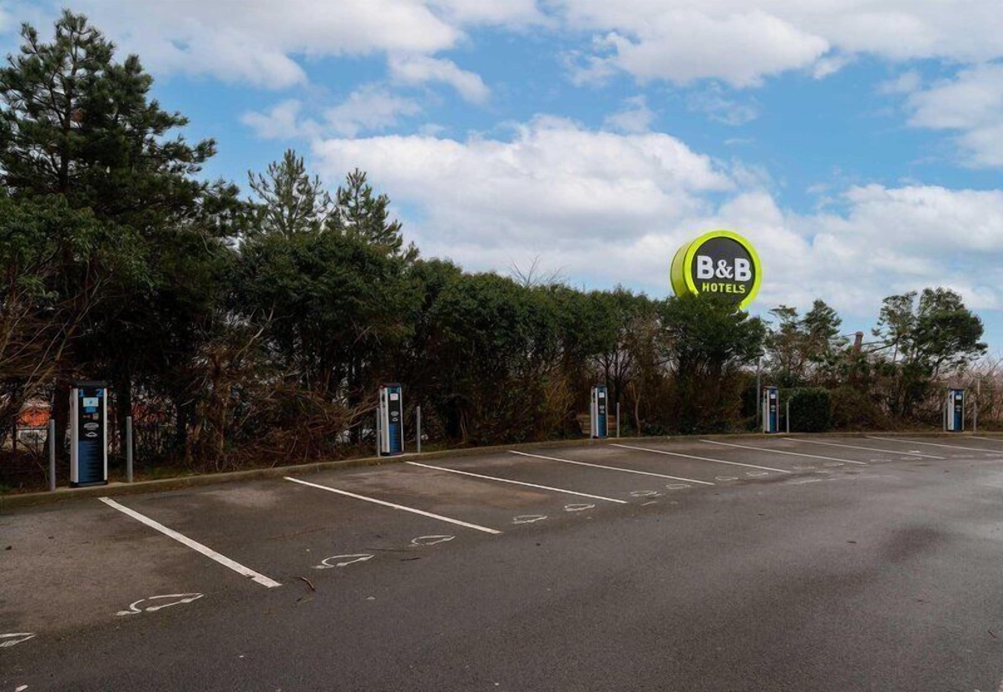 A B&B hotel parking lot with marked parking spaces and a sign indicating the hotel name.