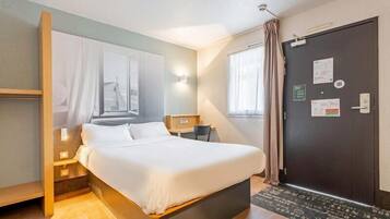 A hotel room with a bed, bedside tables, a window, a door, and a view of the outside.