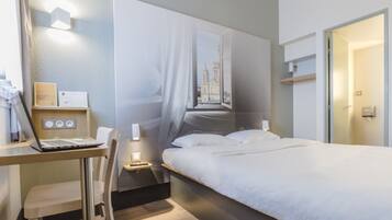 Habitación de hotel moderna con una cama, un escritorio con una computadora portátil y vistas a un edificio a través de una ventana.