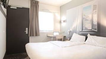 Una habitación de hotel con una cama grande, un escritorio con computadora, una silla y un ventanal con cortinas.
