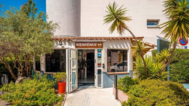 Un edificio con un letrero que dice 'BIENVENUE', una entrada accesible para sillas de ruedas y un camino que lleva a la entrada.