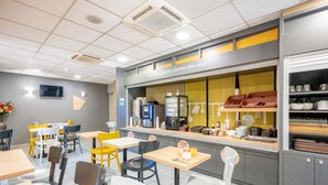 Una cafetería con mesas y sillas, una barra con una máquina de café y un televisor en la pared.