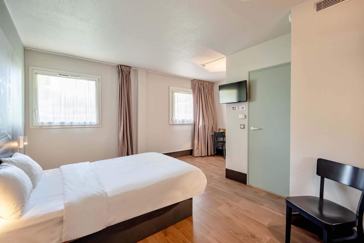 Et hotelværelse med en seng, en stol, et fjernsyn og et skrivebord.