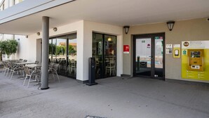 Entrada de hotel con mesas al aire libre, un dispositivo de pago y una puerta de vidrio.