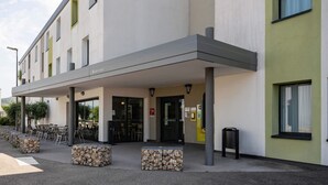 Un edificio moderno con entrada cubierta, mesas al aire libre y un letrero que dice "Bienvenue".