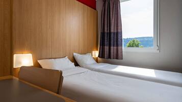 Ein Hotelzimmer mit zwei Einzelbetten, einem Holzkopfteil, einem Tisch und einem Fenster mit Vorhängen.
