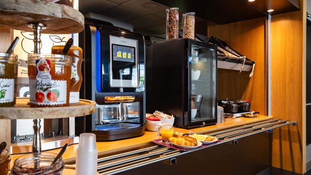 Una barra de desayuno con una máquina de café, frascos de mermeladas y una variedad de productos para el desayuno.