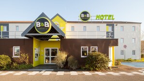 Et B&B hotel med et moderne design, tydelig B&B logo, en gul facade og en klar indgang.