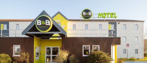 Un hôtel de la chaîne B&B au design moderne, caractérisé par un logo B&B bien visible, une façade jaune et une entrée clairement identifiable.