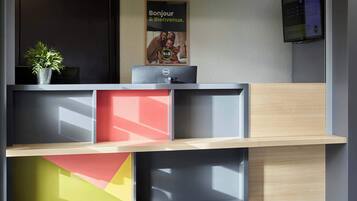 Un mostrador de recepción con un monitor de computadora, una planta en maceta y un cartel en la pared.