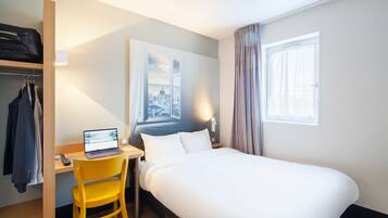 A hotel room with a bed, a desk with a laptop, a chair, a wardrobe, and a window with curtains.