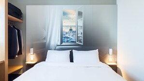 Et hotelværelse med en seng, to sengeborde med lamper, et klædeskab og et stort vindue med udsigt over bybilledet.