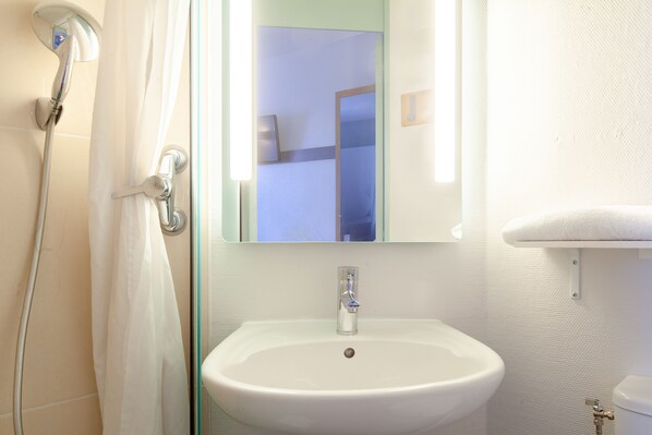 A bathroom with a white sink, a shower, and a mirror above the sink. - B&B HOTEL Maurepas (Maurepas)