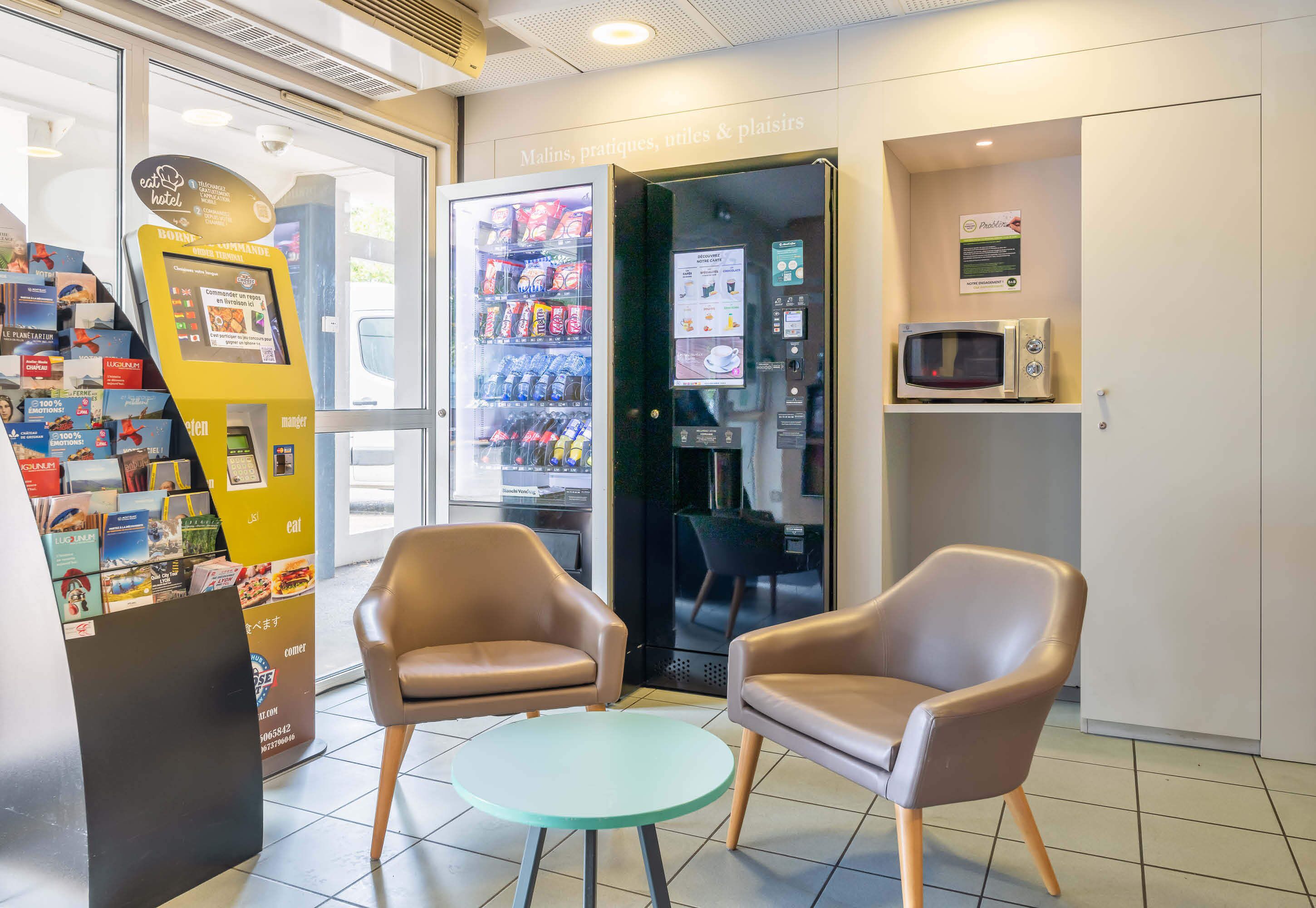 A hotel lobby with a vending machine, two leather chairs, a small table, and a microwave on a shelf.