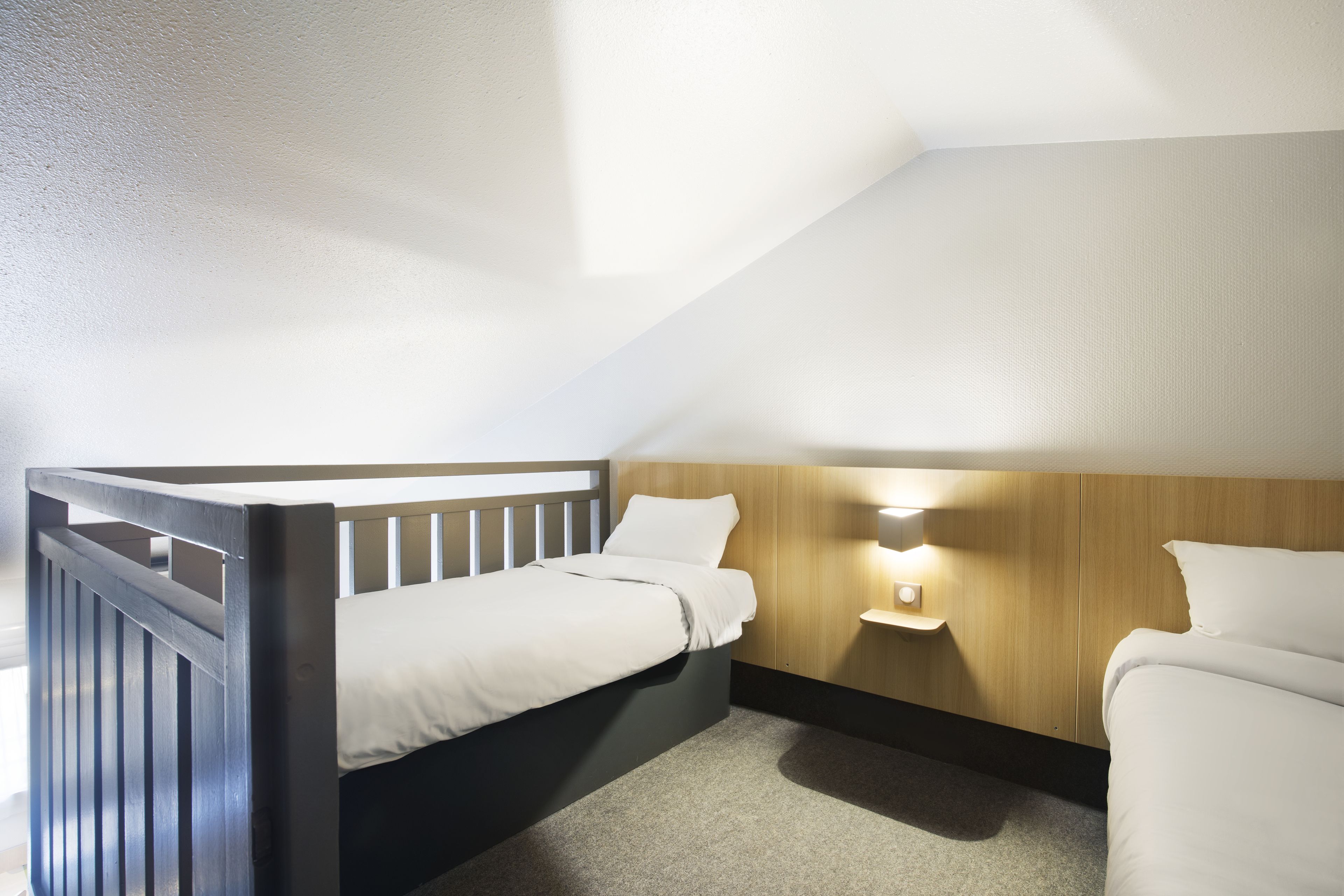 A compact room with a single bed, a small bedside table, and a wall-mounted light fixture.