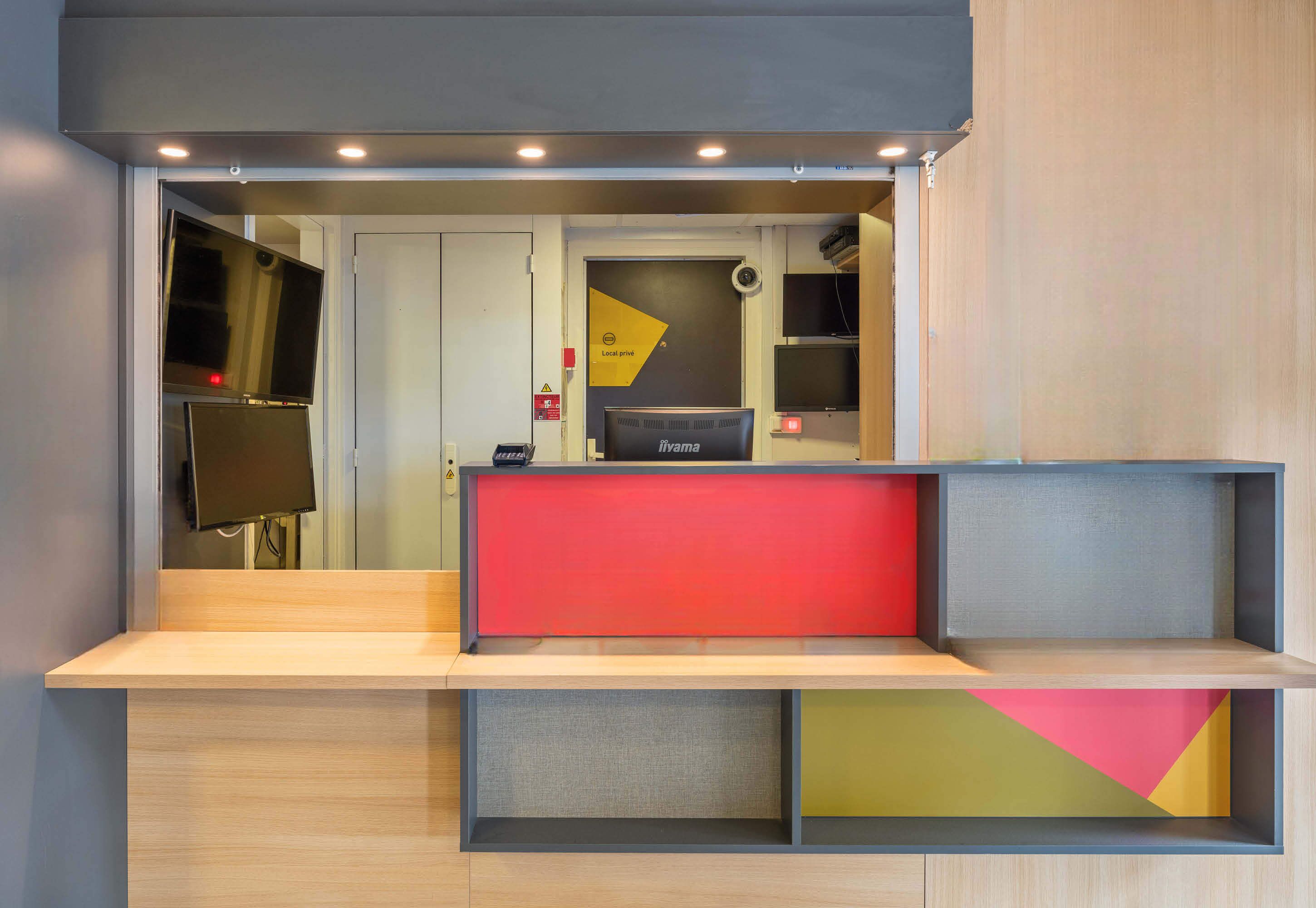 A reception desk with a red panel, a black monitor, and a sign that reads "Local pub."