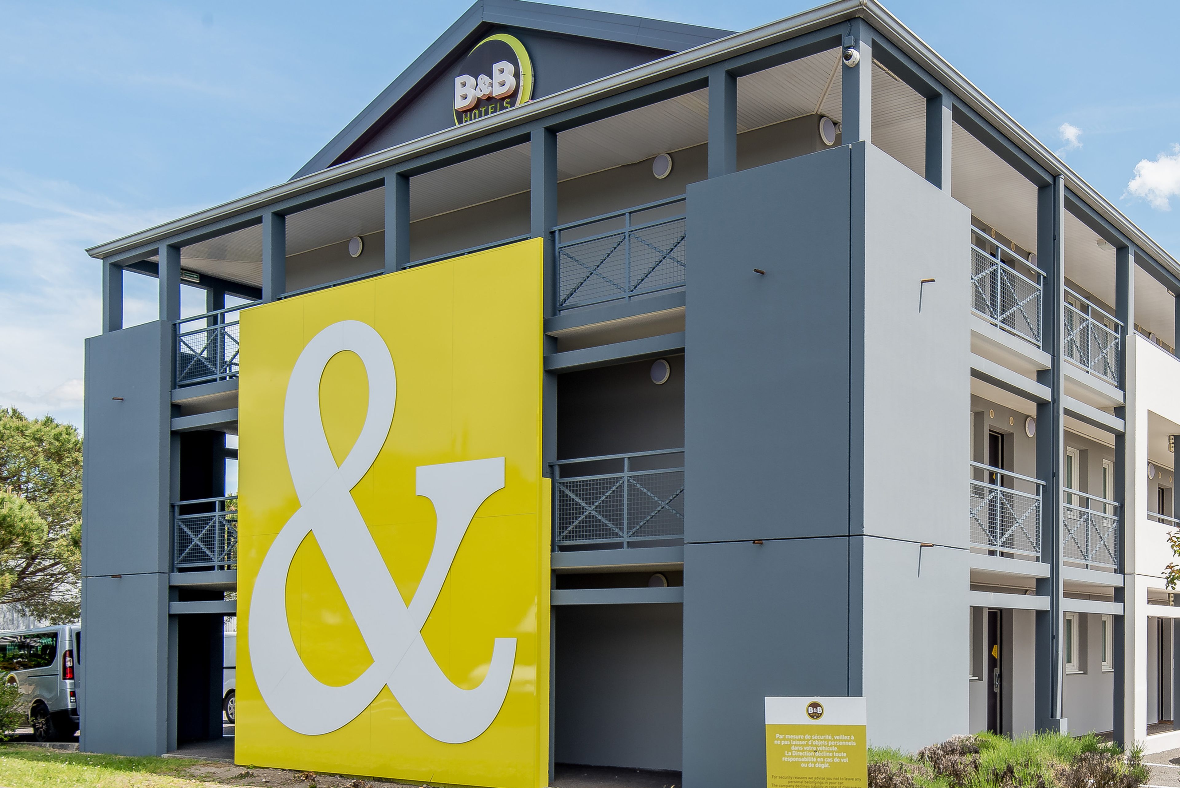 A B&B hotel with a prominent yellow and white sign, multiple balconies, and a modern architectural design.