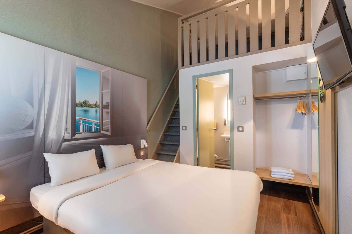 A hotel room with a large bed, a view of a lake, a staircase, and a walk-in closet.