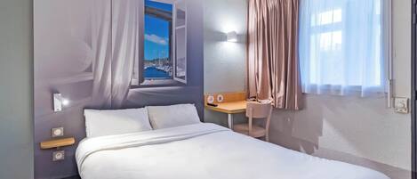 Habitación de hotel con cama, escritorio, silla, ventana con cortinas e iluminación en la pared.