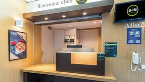 Een receptiebalie met een houten toonbank, een digitaal scherm erboven en een bordje met de tekst 'Bienvenue chez B&B HOTELS'.