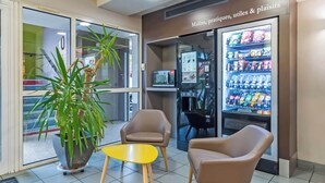 Een zithoek met twee stoelen en een kleine tafel, een automaat met snacks, en een kamerplant.